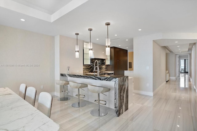 kitchen with light tile floors, a kitchen bar, stone countertops, white cabinets, and hanging light fixtures