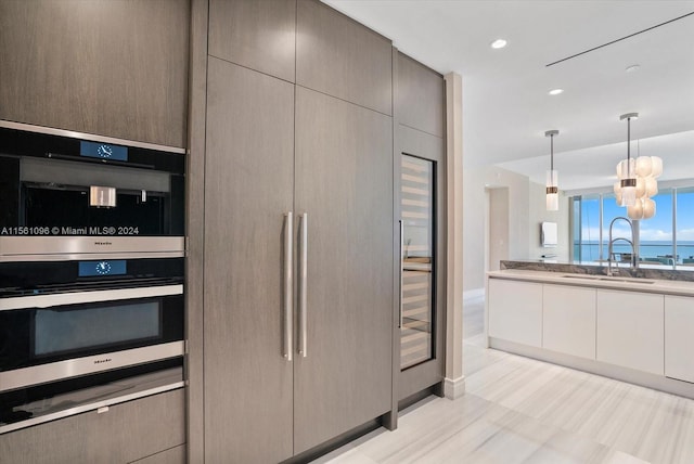 kitchen featuring sink, double oven, light stone countertops, decorative light fixtures, and a notable chandelier