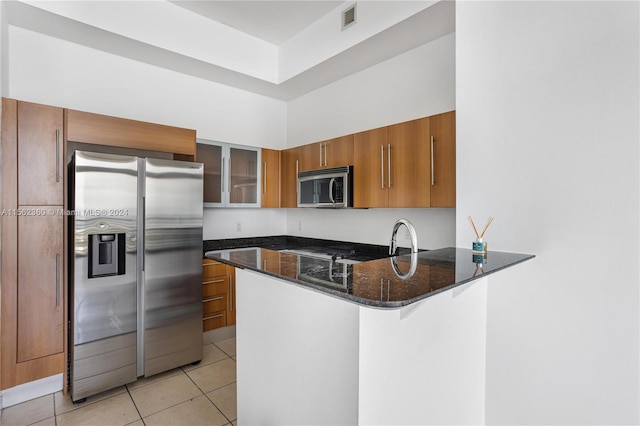 kitchen with dark stone counters, stainless steel appliances, light tile floors, and kitchen peninsula