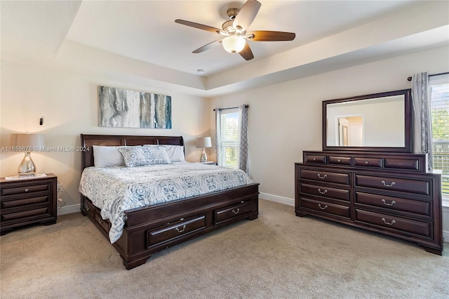 bedroom with light colored carpet, a tray ceiling, ceiling fan, and multiple windows