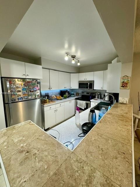 kitchen with sink, light tile floors, appliances with stainless steel finishes, track lighting, and white cabinetry