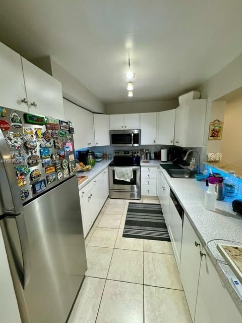 kitchen with stainless steel appliances, light tile flooring, white cabinetry, and sink