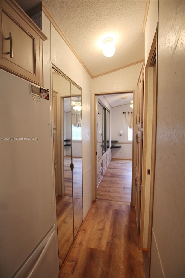 hall featuring a textured ceiling, dark wood-type flooring, crown molding, and vaulted ceiling