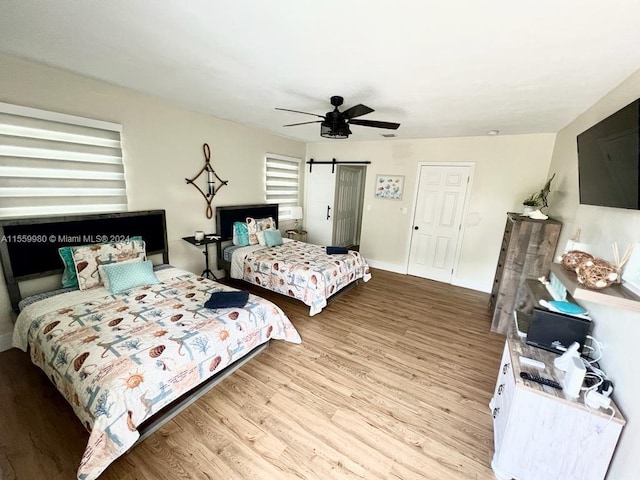 bedroom with a barn door, ceiling fan, and light wood-type flooring