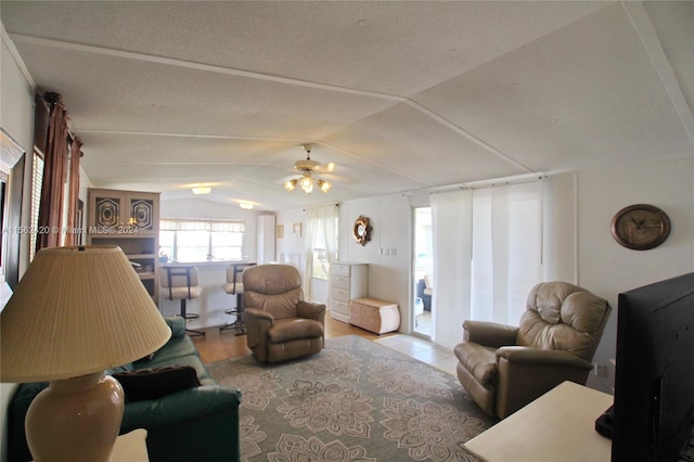 living room with lofted ceiling, ceiling fan, light wood-type flooring, and a textured ceiling