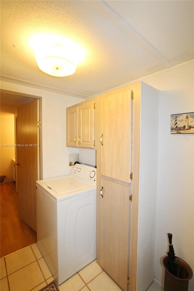 laundry room featuring a textured ceiling, cabinets, light tile floors, and washer / dryer