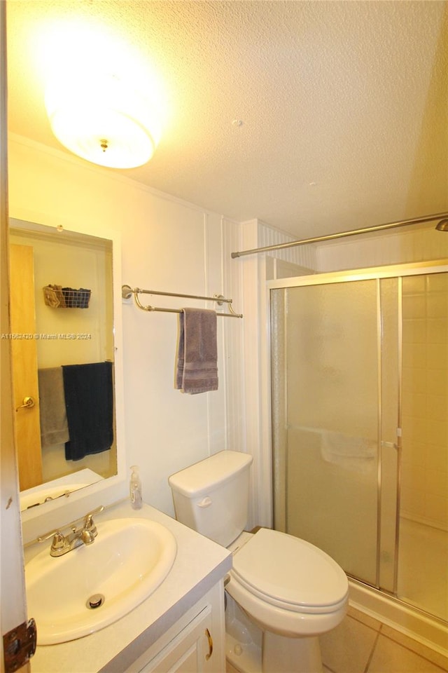 bathroom featuring tile flooring, a textured ceiling, an enclosed shower, toilet, and vanity