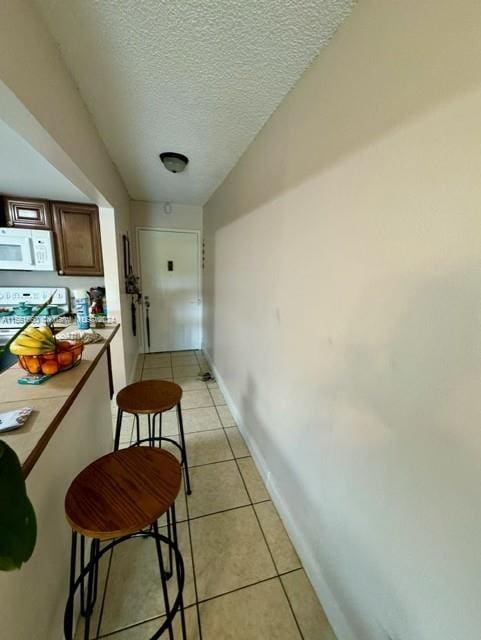 hallway with a textured ceiling and light tile floors