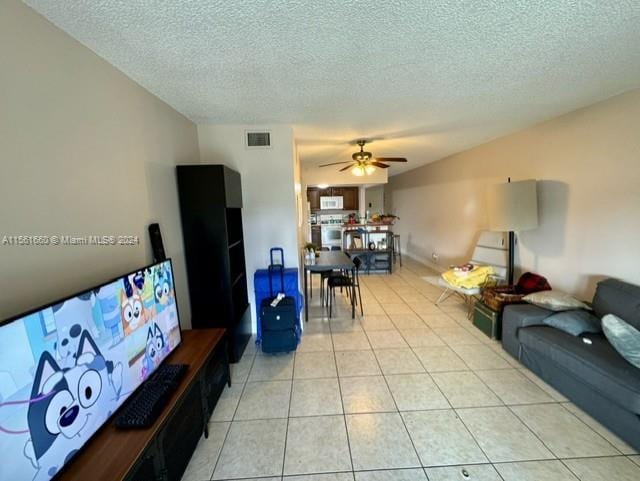 living room featuring light tile flooring, ceiling fan, and a textured ceiling