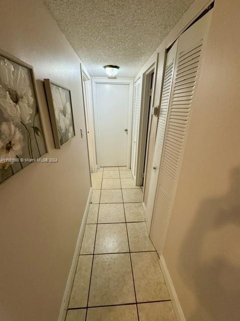 corridor featuring a textured ceiling and light tile flooring