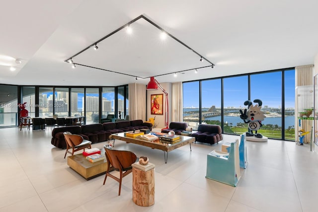 living room featuring light tile flooring, a water view, rail lighting, and a wall of windows