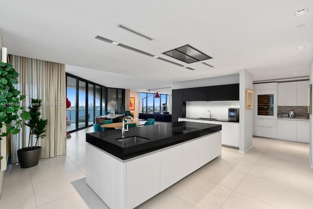 kitchen featuring light tile flooring, a wall of windows, and an island with sink