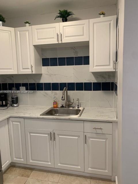 kitchen featuring light stone counters, light tile floors, white cabinets, sink, and tasteful backsplash