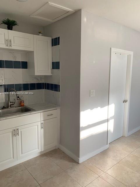 kitchen with sink, tasteful backsplash, light tile flooring, and white cabinetry