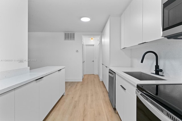 kitchen with appliances with stainless steel finishes, sink, white cabinetry, and light hardwood / wood-style floors