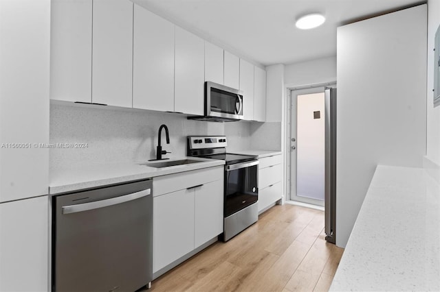 kitchen featuring light wood-type flooring, white cabinets, tasteful backsplash, and stainless steel appliances