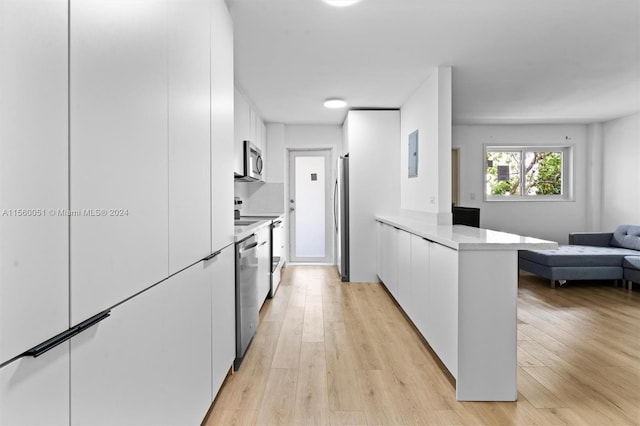 kitchen with light stone countertops, kitchen peninsula, light hardwood / wood-style floors, stainless steel appliances, and white cabinets