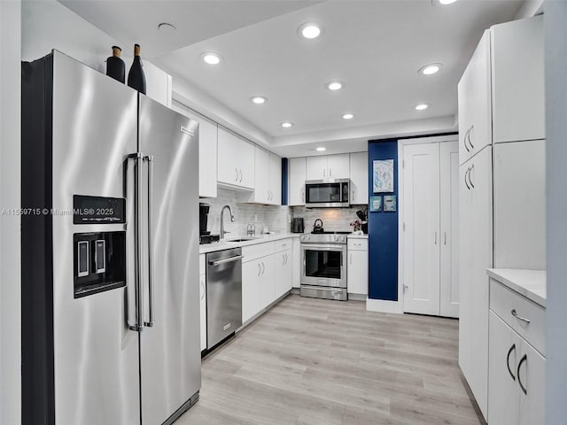 kitchen with sink, light hardwood / wood-style flooring, appliances with stainless steel finishes, tasteful backsplash, and white cabinetry