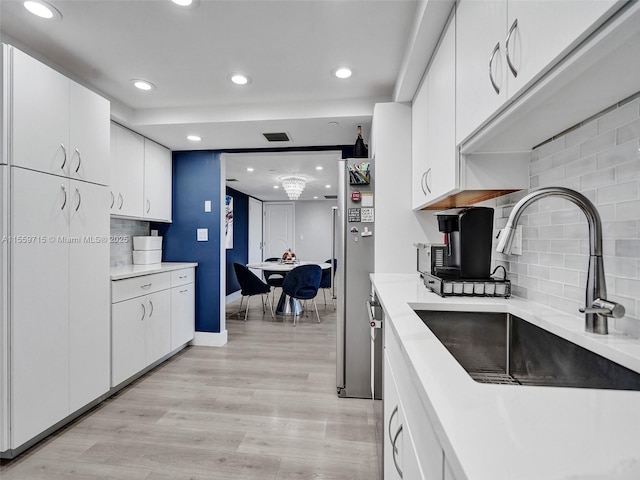 kitchen with tasteful backsplash, light hardwood / wood-style floors, sink, white cabinets, and a chandelier