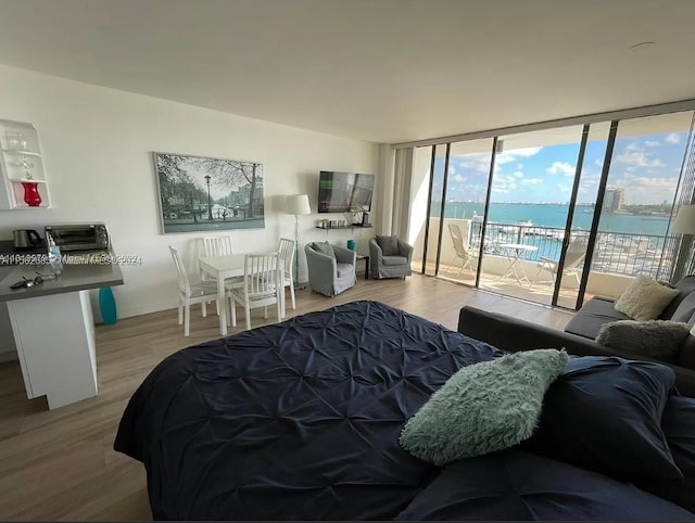 bedroom with hardwood / wood-style floors, expansive windows, access to exterior, and a water view