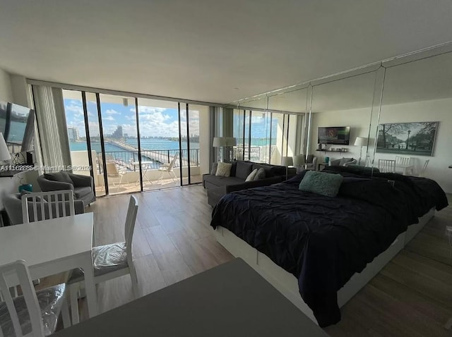 bedroom featuring a water view, expansive windows, hardwood / wood-style floors, and access to outside