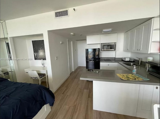 kitchen featuring kitchen peninsula, light hardwood / wood-style flooring, white cabinetry, stainless steel microwave, and black fridge