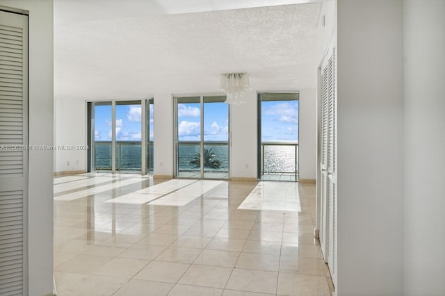 unfurnished room featuring expansive windows, a textured ceiling, light tile patterned floors, and a water view