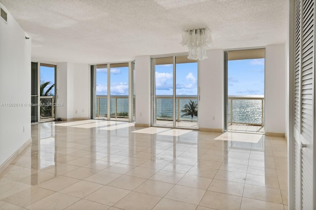 tiled empty room featuring a textured ceiling, floor to ceiling windows, and a water view