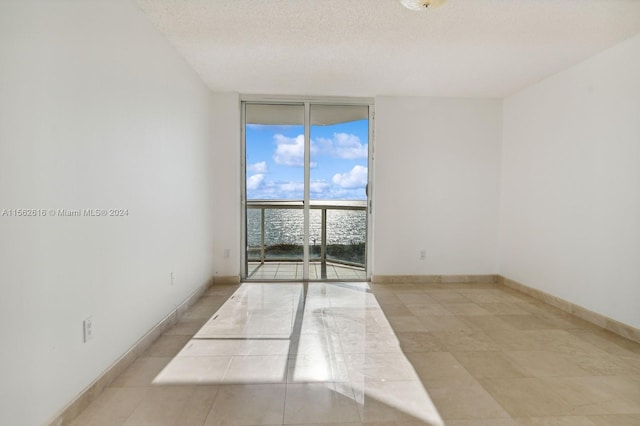 tiled empty room with a textured ceiling and floor to ceiling windows