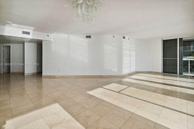 tiled spare room with a textured ceiling and a chandelier