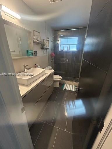 bathroom featuring toilet, a tile shower, vanity, and tile flooring