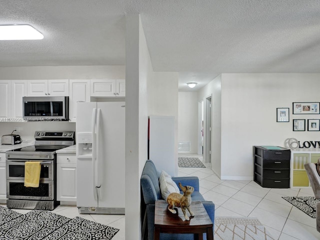 kitchen with light tile floors, appliances with stainless steel finishes, white cabinetry, and a textured ceiling