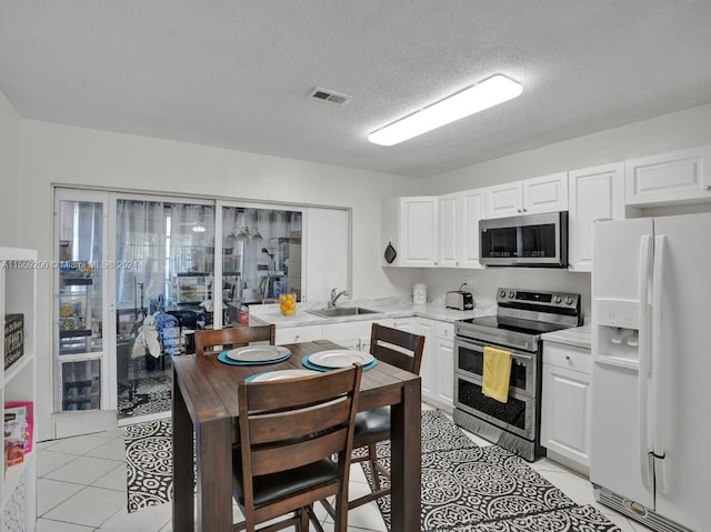 kitchen with appliances with stainless steel finishes, sink, light tile floors, white cabinets, and a textured ceiling