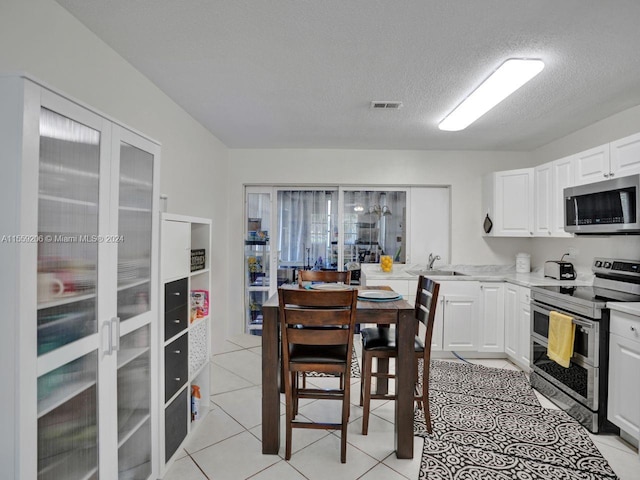 kitchen with light tile flooring, a textured ceiling, white cabinets, and appliances with stainless steel finishes