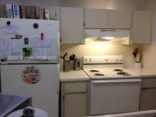 kitchen with cream cabinetry, light tile floors, white fridge, and stove