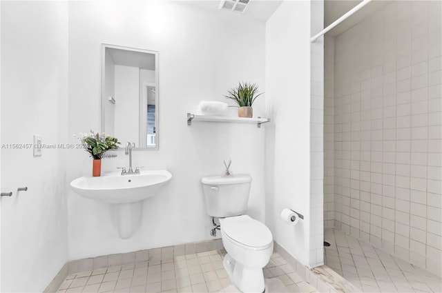 bathroom with toilet, tile patterned floors, and a tile shower