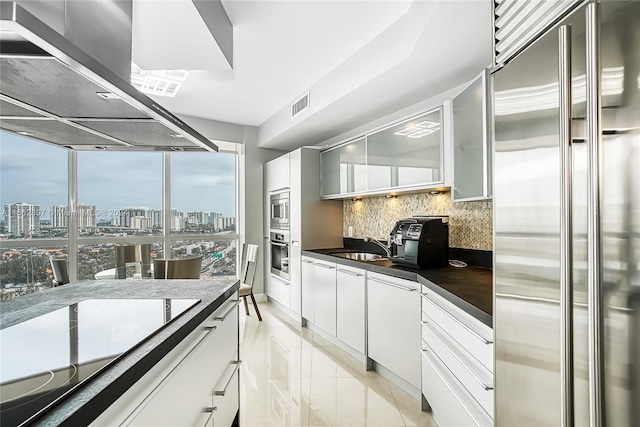 kitchen featuring extractor fan, backsplash, light tile floors, white cabinets, and built in appliances