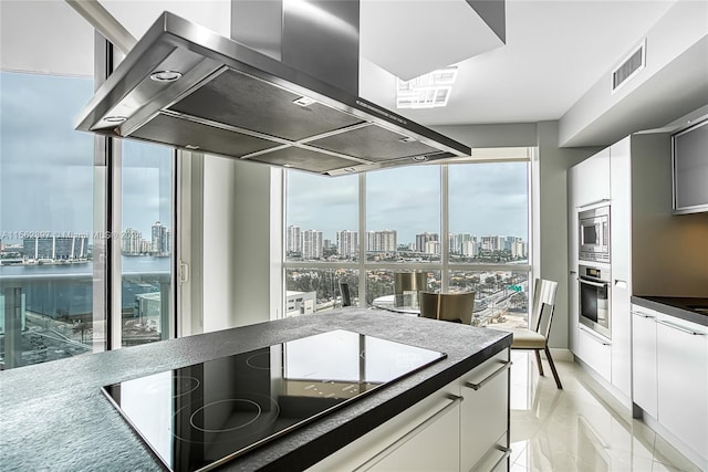 kitchen with island range hood, light tile flooring, expansive windows, appliances with stainless steel finishes, and white cabinets