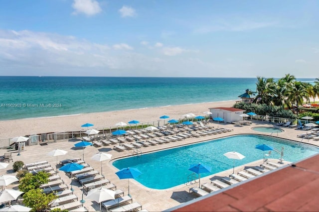 view of swimming pool with a patio area, a water view, and a beach view