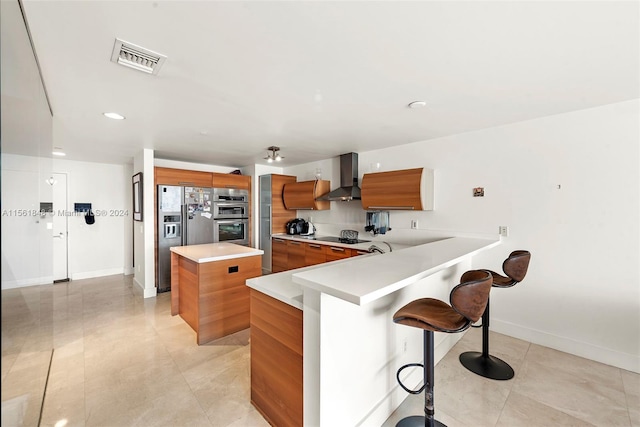 kitchen featuring a kitchen breakfast bar, appliances with stainless steel finishes, light tile floors, and wall chimney range hood