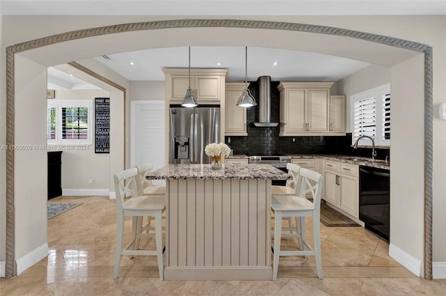 kitchen featuring wall chimney exhaust hood, appliances with stainless steel finishes, cream cabinets, light tile floors, and light stone counters