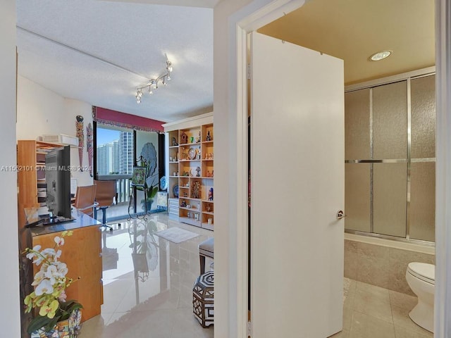 bathroom featuring tile flooring, combined bath / shower with glass door, toilet, and rail lighting