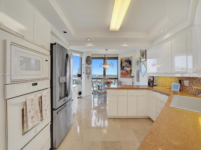 kitchen featuring pendant lighting, white appliances, white cabinetry, and a raised ceiling