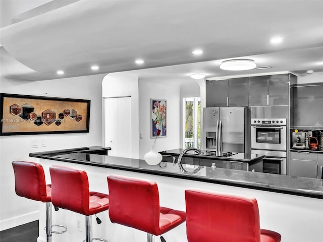 kitchen with a kitchen breakfast bar, appliances with stainless steel finishes, gray cabinetry, and dark stone counters