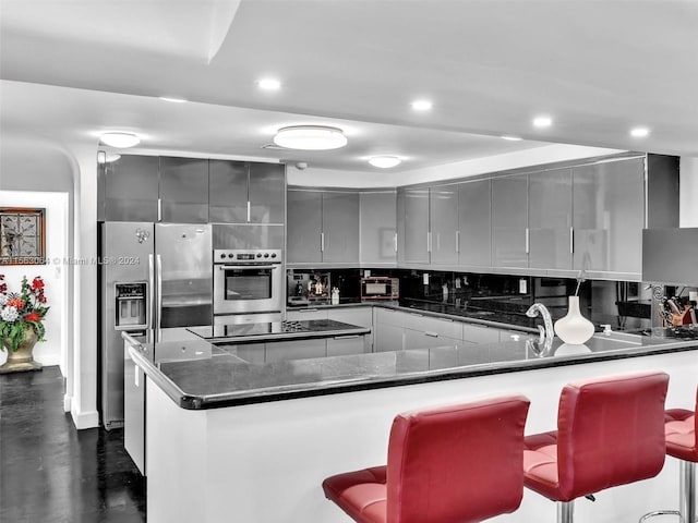 kitchen with stainless steel appliances, kitchen peninsula, a breakfast bar area, gray cabinetry, and backsplash