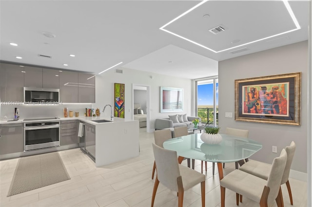 kitchen with kitchen peninsula, gray cabinetry, stainless steel appliances, sink, and light hardwood / wood-style flooring