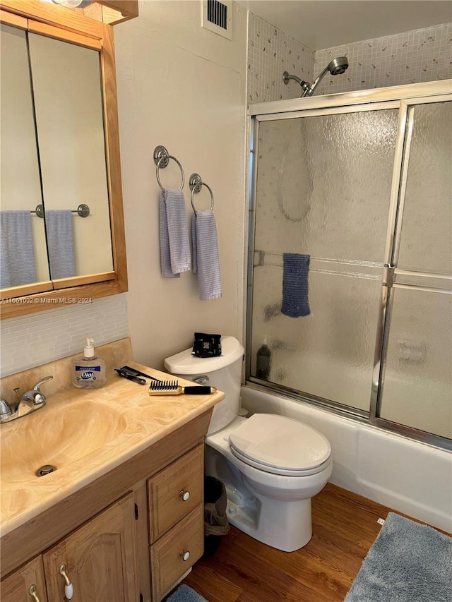 full bathroom with hardwood / wood-style flooring, vanity, combined bath / shower with glass door, and toilet