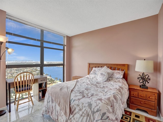 bedroom with a wall of windows, a textured ceiling, and a water view