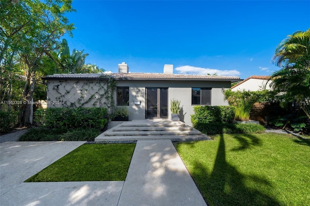 view of front of house with a front yard, french doors, a chimney, and stucco siding