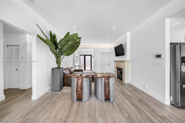 interior space with a tiled fireplace, baseboards, light wood-style floors, and stainless steel refrigerator with ice dispenser